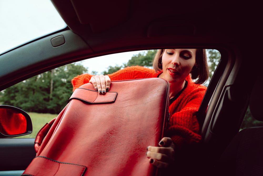 Woman putting suitcase in front window of car