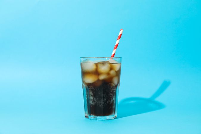 Glass with cold cola and tubule on blue background, space for text