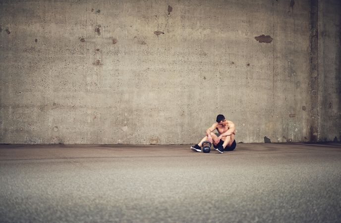 Muscular man sitting in large concrete room next to kettlebell
