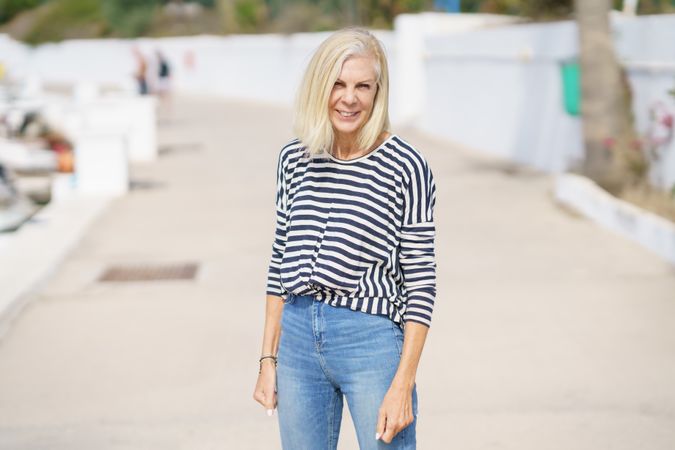Older woman in jeans and striped shirt standing outside on sunny day