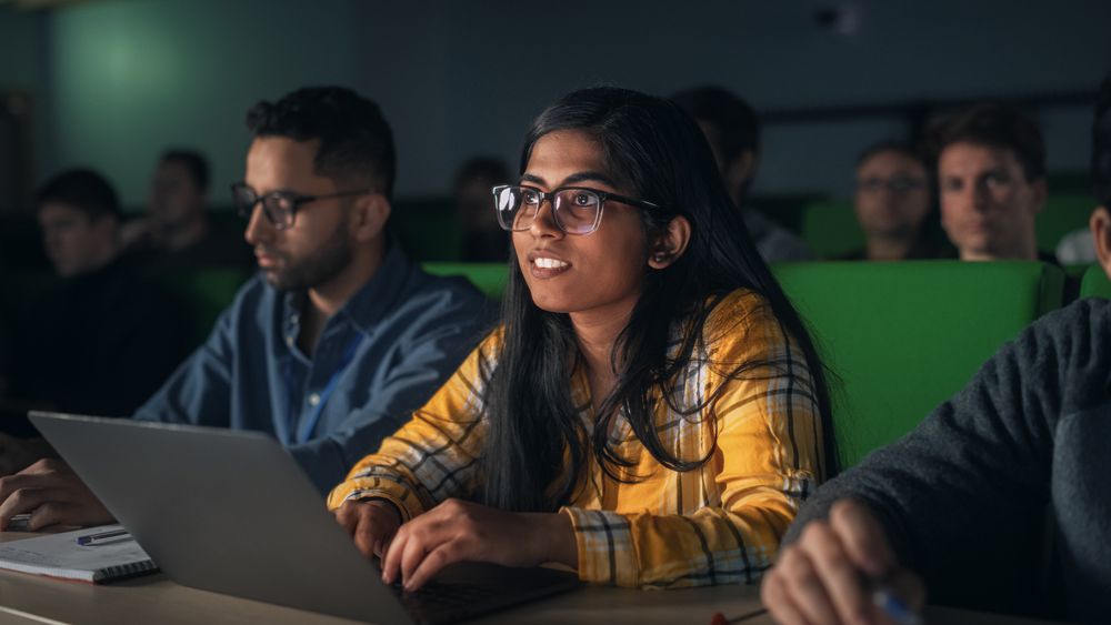 Young Woman Using Laptop Computer and Taking Notes During the Lecture