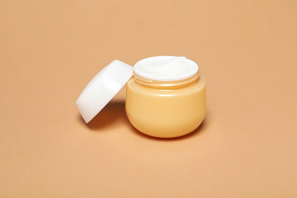 Jar with cream on beige background, close up