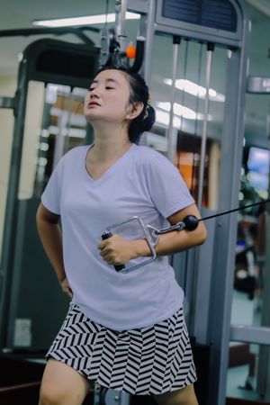 a woman using a cable machine inside a gym.
