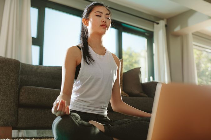Chinese woman practicing yoga with laptop at home.