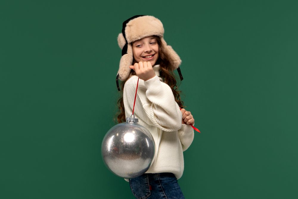 Smiling girl in winter hat holding large silver ornament.