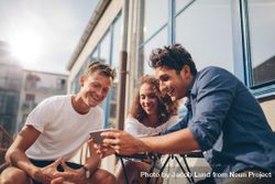 Three young friends sitting outdoors and looking at mobile phone 4dPql4