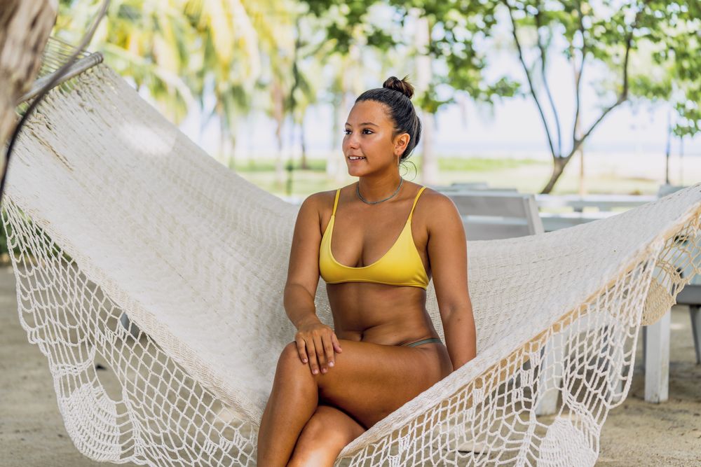 Joyful woman in bikini resting in hummock on beach