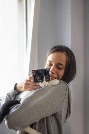 A young woman hugs and plays with her black and white cat while at home