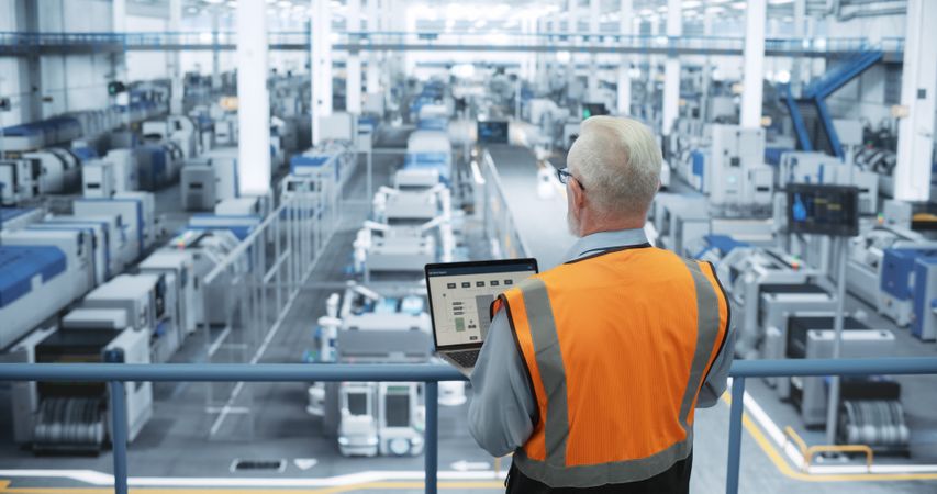 Portrait of a Thoughtful Engineer Monitoring and Analyzing Conditions at a Modern Electronics Factory with Automated Robots Working with the Help of Artificial Intelligence Software