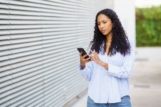 A young woman in casual attire uses her smartphone outdoors, showing a modern, confident lifestyle