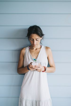 Portrait of woman with ponytail checking phone while leaning on wood wall