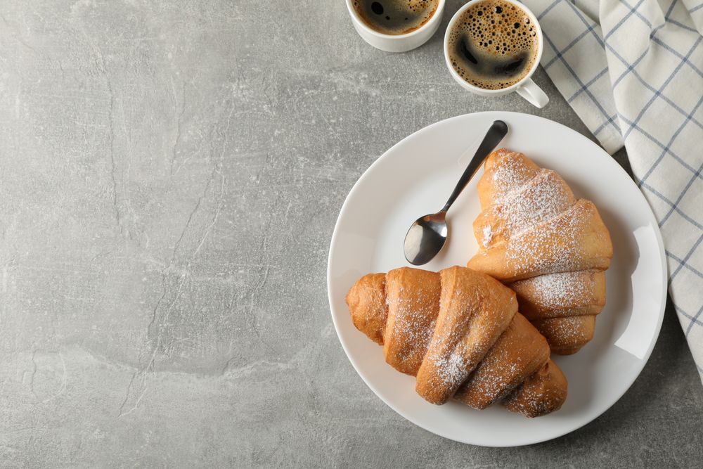 Plate with croissants, cups of coffee and towel on grey table, copy space