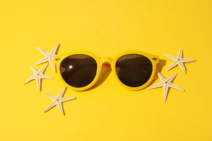 Starfishes and sunglasses on yellow background, top view