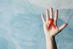Hand and red awareness ribbon against blue background, space for text