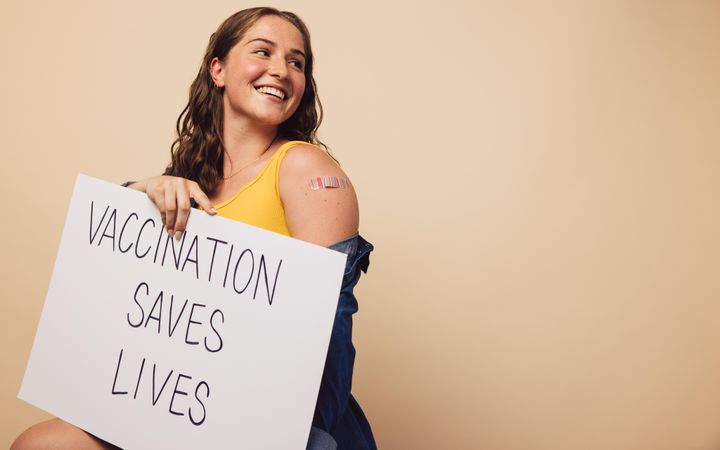Cheerful woman holding a signboard with "vaccination saves lives" written on it