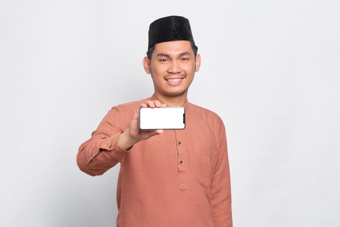 Happy Muslim man in kufi hat presenting mobile phone with light screen
