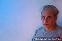 Portrait of middle aged man in gray shirt with questing look against light background in UV lit studio 4M7Zy0