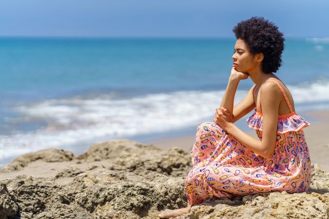 Woman sitting on the rocks on the coast looking thoughtfully out to the ocean view