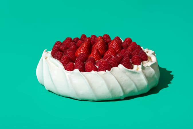Pavlova cake topped with fresh berries, isolated on a green background