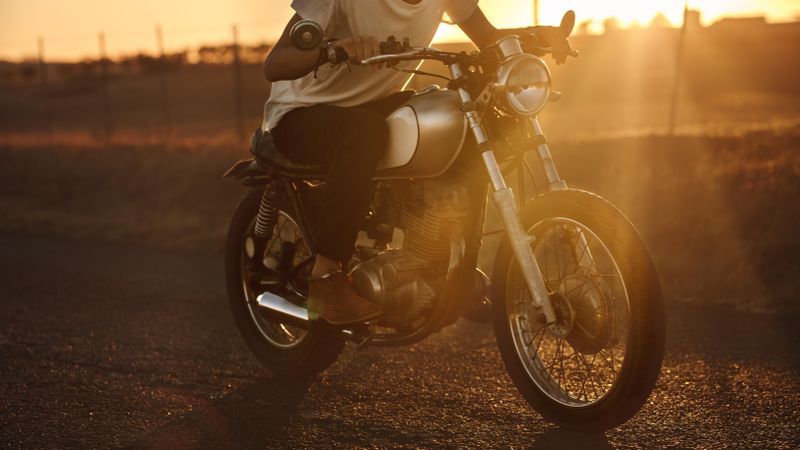 Man driving a motorbike fast through country road at sunset