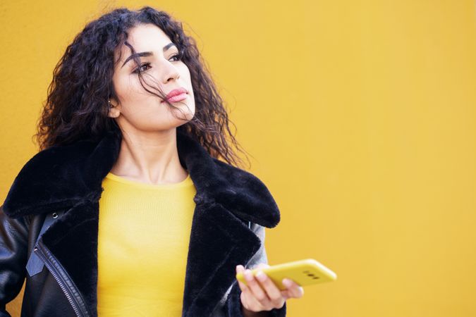 Female standing with yellow phone in front of yellow background