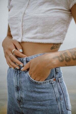 Cropped image of tattooed woman wearing crop top and denim pants