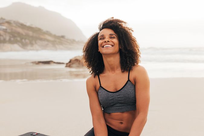 Happy woman sitting on beach in workout gear