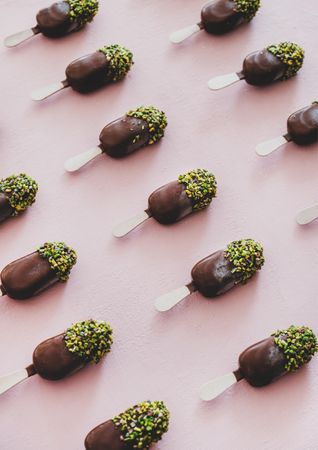 Diagonal rows of ice cream chocolate pistachio popsicles, pink background, vertical composition