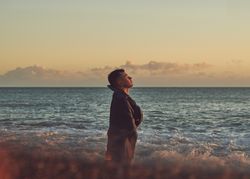 Young man standing near the ocean with his eyes closed