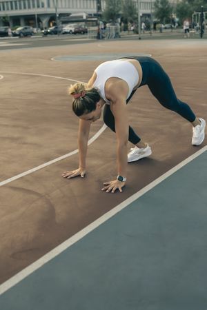 Determined woman in a starting pose for a calisthenics or HIIT workout on an urban basketball court