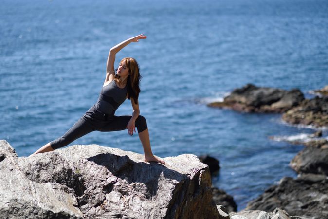 Young woman doing yoga on the rocks at the beach