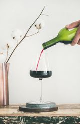 Wine glass being poured from bottle with dried cotton in vase, vertical composition