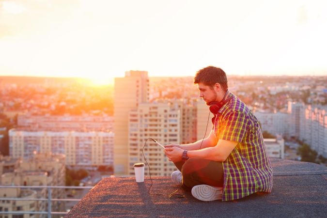 Male sitting on roof with tablet and coffee