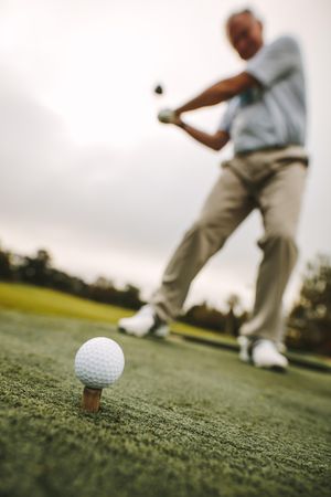 Golf ball on tee with male player practicing a shot at driving range