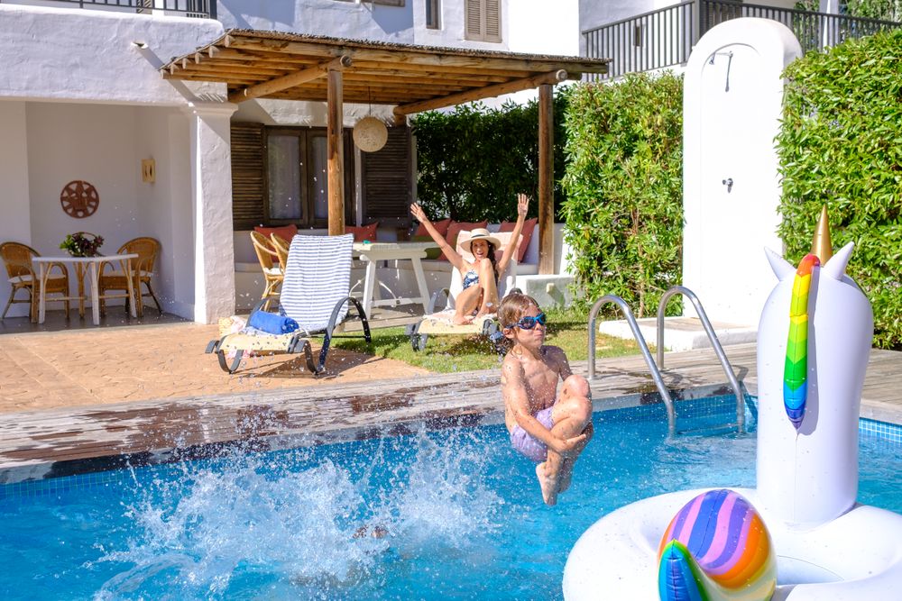 Active child jumping into swimming pool near mom relaxing on sun