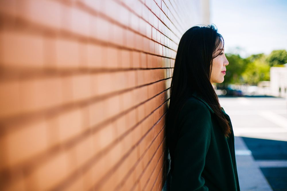 Pensive Asian woman leaning on brick wall