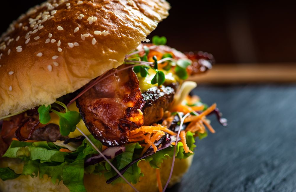 American hamburger with meat, cheese and different vegetables on dark rustic background with copy space