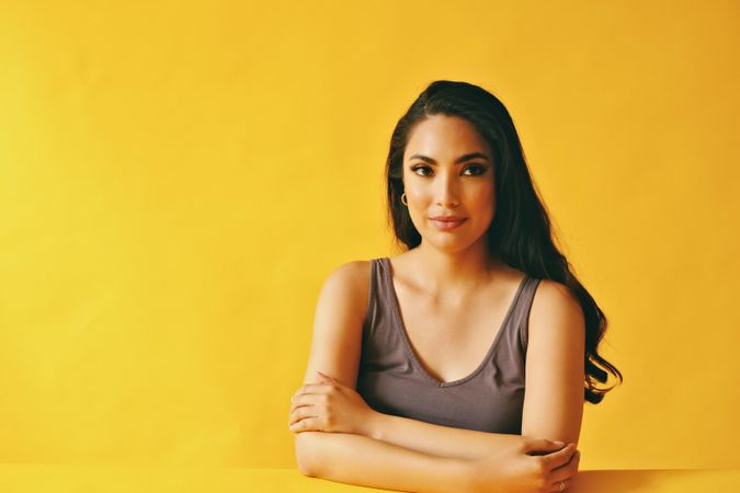 Pensive Hispanic woman looking away from camera and sitting in yellow room, copy space