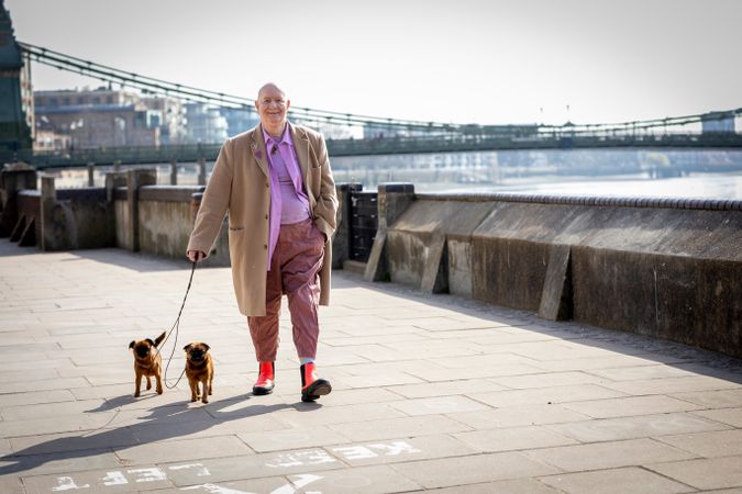 Happy older man walking by river with two small dogs