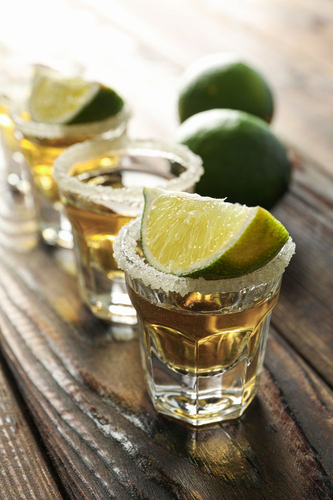 Tequila shots with salt and lime slices on wood table, closeup