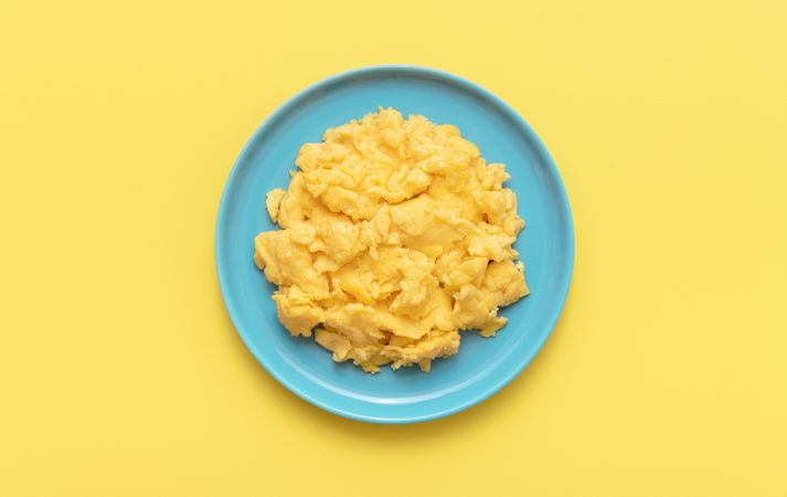 Scrambled eggs on a blue plate, top view on a yellow table