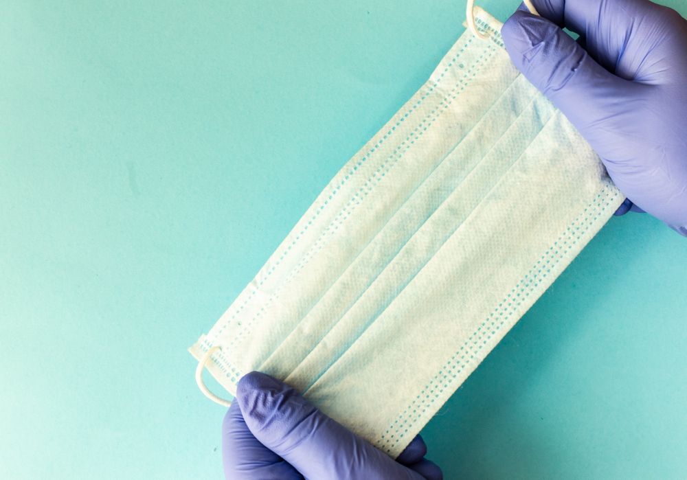 Covid-19 virus concept of hands in latex gloves holding facemask on blue background