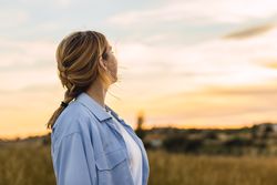young blonde woman on a field looking sunset