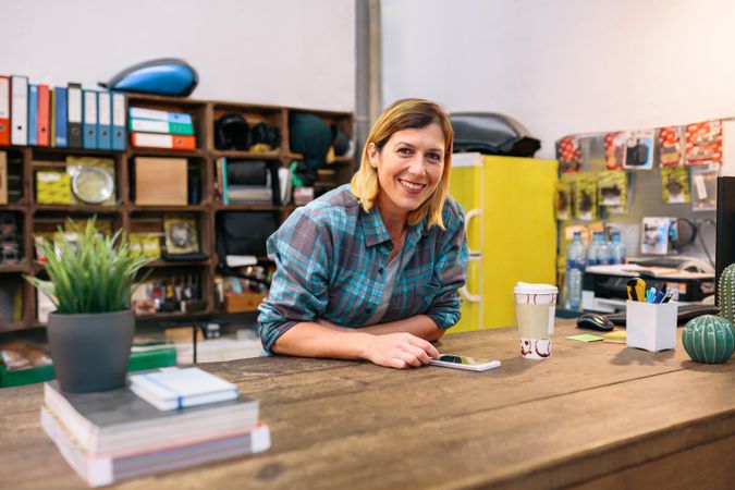 Portrait of happy blonde woman entrepreneur looking at camera in local motorbike shop.