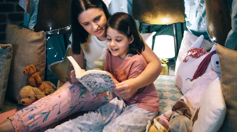 Girl reading with her mother in a makeshift tent