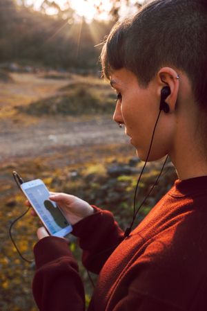 Young woman with piercing listening music on smartphone on hill