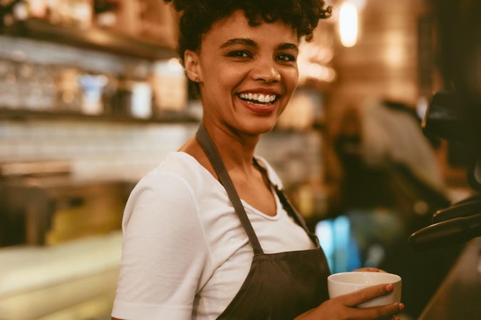 Female barista holding a cup standing by coffee maker