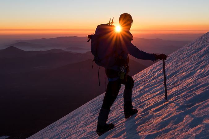 Silhouette of person climbing snow covered steep during sunset
