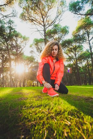 Woman tying shoelaces on meadow in sunlight