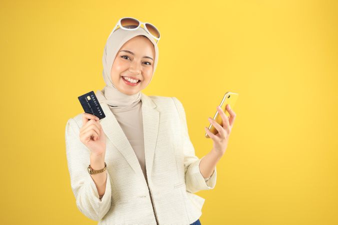 Smiling Young Asian Muslim Woman Holding Mobile Phone and Credit Card